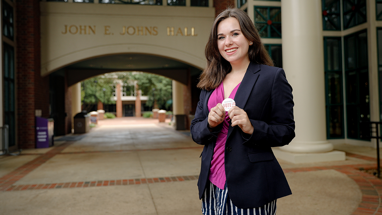 Erica Daly '22 holds a Dins Vote pin in front of Johns Hall