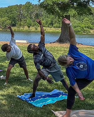 Students practice a yoga pose by the side of Furman Lake.